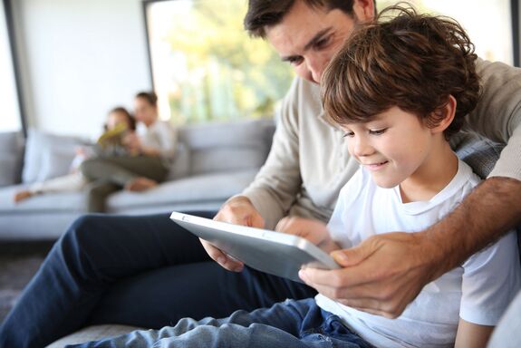 Ein Junge und sein Vater schauen begeistert auf den Bildschirm eines Tablets.