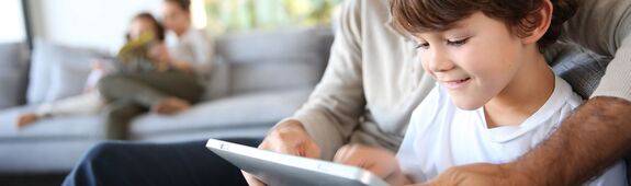 Ein Junge und sein Vater schauen begeistert auf den Bildschirm eines Tablets.