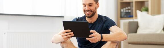 Ein Mann in Sportkleidung schaut freudig auf den Bildschirm