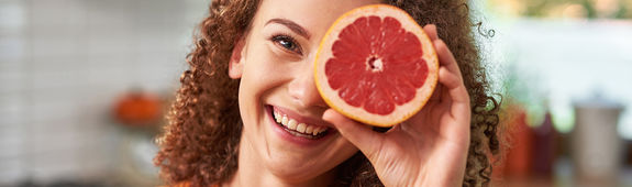 Eine Frau hält eine Orange vor ihr Auge.