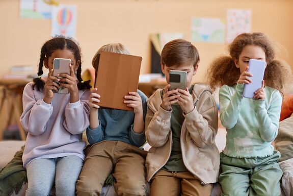 Vier Kinder die auf Handy oder Tablet starren