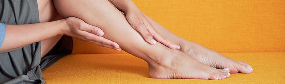 Eine Frau streicht mit den Händen über Ihr Fußgelenk.